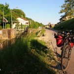 Fahrrad mit roten Packtaschen auf dem Kanalradweg. Sonne wirft lange Schatten.