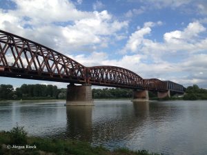 Fachwerk-Eisenbahnbrücke über den Rhein, Bogen, graublauer Himmel, der Fluss. Rostbraun